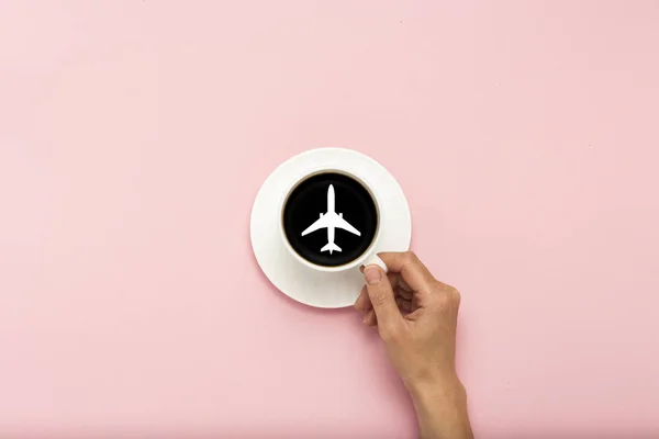 Main féminine tenant une tasse blanche avec du café noir sur un fond rose. Panneau d'avion. Couché plat, vue du dessus — Photo