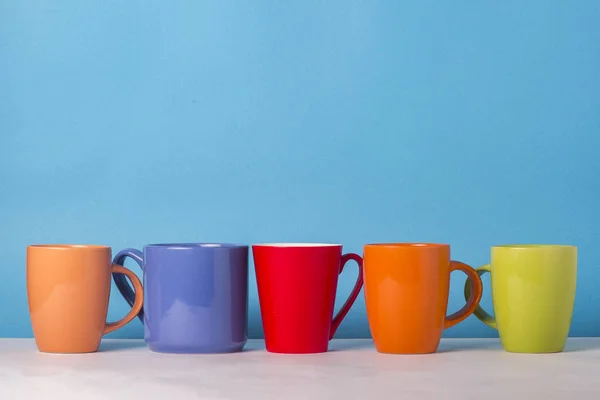 Many multicolored cups of coffee or tea on a blue background. The concept of a friendly company, a large family, meeting friends for a cup of tea or coffee