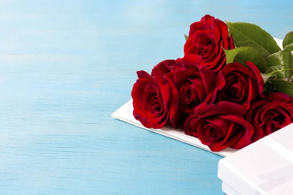 Ramo de rosas rojas, caja de regalo blanca, fondo de madera azul. Co — Foto de Stock
