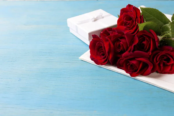 Ramo de rosas rojas, caja de regalo blanca, fondo de madera azul. Co — Foto de Stock