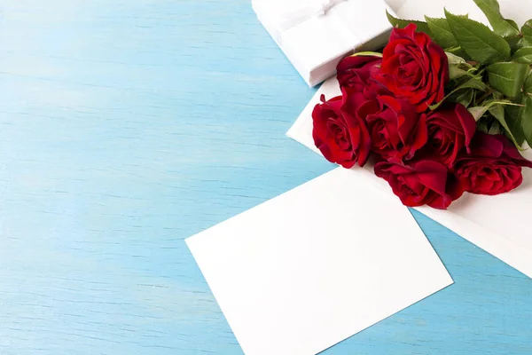 Ramo de rosas rojas Caja de regalo blanca hoja limpia, respaldo de madera azul — Foto de Stock