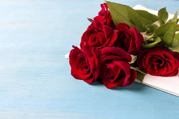 Ramo de rosas rojas en una servilleta blanca y fondo de madera azul — Foto de Stock