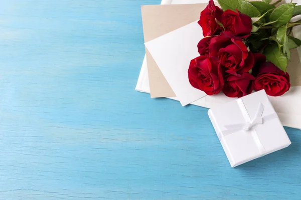 Ramo de rosas rojas Caja de regalo blanca hoja limpia, respaldo de madera azul — Foto de Stock