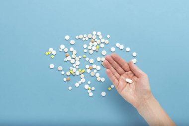 Avuç içinde dağınık hapları ile mavi bir arka plan üzerinde bir hap tutan el. Hastalık, pharmacetiya, ilaç durumunda uyuşturucu alarak kavramı. Doğru ilaç seçimi. Düz yatıyordu, en iyi görünümü