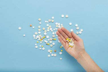 Avuç içinde dağınık hapları ile mavi bir arka plan üzerinde bir hap tutan el. Hastalık, pharmacetiya, ilaç durumunda uyuşturucu alarak kavramı. Doğru ilaç seçimi. Düz yatıyordu, en iyi görünümü