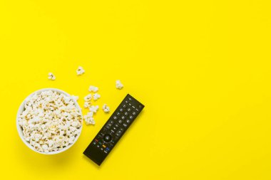 Patlamış mısır ve Tv sarı bir arka plan üzerinde uzak bir kase. Tarassut Tv, film, Tv dizisi, spor, kavramı gösterir. Düz yatıyordu, en iyi görünümü.