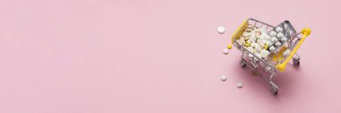 Pembe bir arka plan üzerinde alışveriş arabası hapları ve uyuşturucu dolu marketten. Satın alınan ve tıbbi hazırlıklar, internette satın alabilirsiniz. Düz yatıyordu, en iyi görünümü.