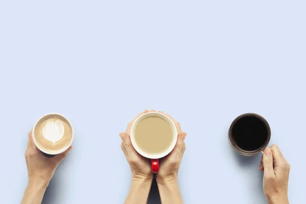 Three pairs of hands are holding cups of coffee on a blue background. Concept breakfast with friends, friendly company. Flat lay, top view