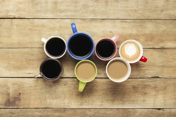Una gran cantidad de tazas multicolores con café y bebidas de café sobre un fondo de madera. Concepto de desayuno con café, café con amigos. Piso tendido, vista superior — Foto de Stock