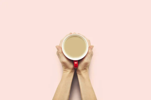 Dos manos sosteniendo una taza con café caliente sobre un fondo rosa. Concepto de desayuno con café o té. Buenos días, noche, insomnio. Piso tendido, vista superior — Foto de Stock