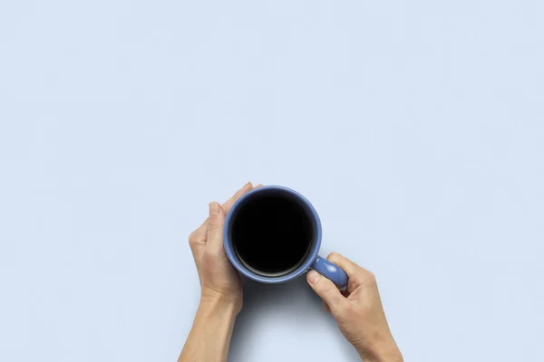 Hand holding a cup with hot coffee on a blue background. Breakfast concept with coffee or tea. Good morning, night, insomnia. Flat lay, top view — Stock Photo, Image