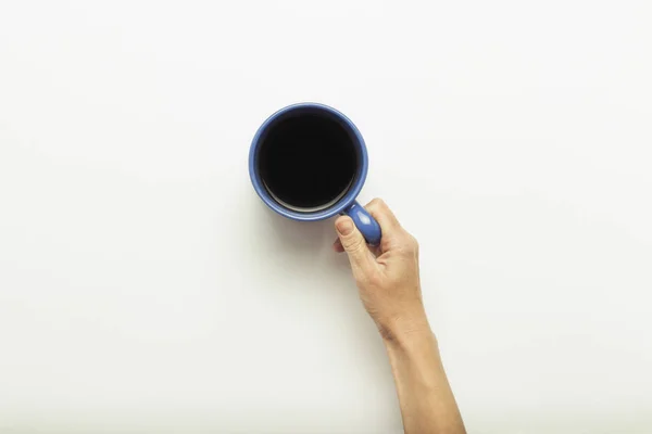 Hand hält eine Tasse mit heißem Kaffee auf blauem Hintergrund. Frühstückskonzept mit Kaffee oder Tee. Guten Morgen, Nacht, Schlaflosigkeit. flache Lage, Draufsicht — Stockfoto