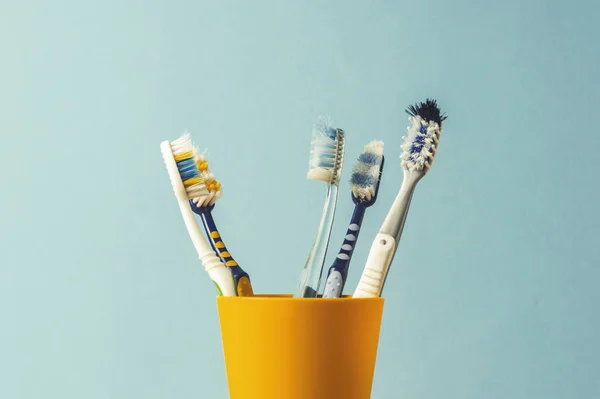 Many toothbrushes in a plastic cup on a blue background. The concept of changing toothbrushes, oral hygiene, dentistry. Big and friendly family. — Stock Photo, Image