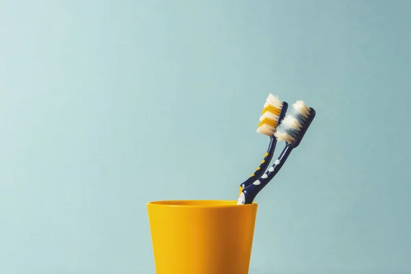 Duas escovas de dentes em um copo de plástico em um fundo azul. O conceito de mudança de escovas de dentes, higiene oral, odontologia. Família jovem e amigável . — Fotografia de Stock