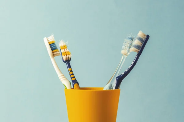 Muitas escovas de dentes em uma xícara de plástico em um fundo azul. O conceito de mudança de escovas de dentes, higiene oral, odontologia. Família grande e amigável . — Fotografia de Stock