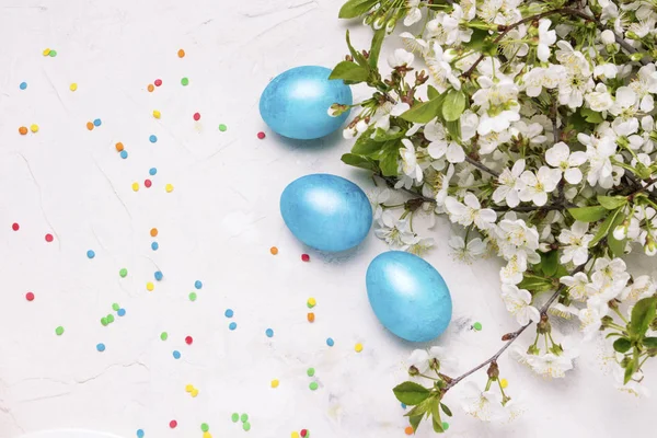 Fioletowy niebieski Wielkanoc jaja, wiosenne kwiaty jabłko, wiśnia, kolorowe cukierki na białym tle kamienia. Widok płaski świeckich, top — Zdjęcie stockowe