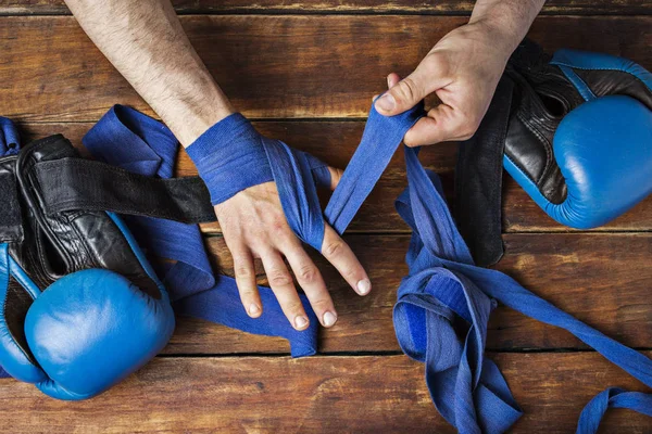 Man bandage boxing tape on his hands before the boxing match on a wooden background. The concept of training for boxing training or fighting. Flat lay, top view