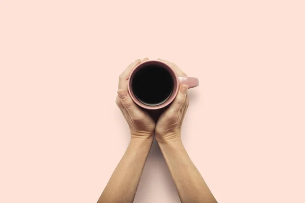 Dos manos sosteniendo una taza con café caliente sobre un fondo rosa. Concepto de desayuno con café o té. Buenos días, noche, insomnio. Piso tendido, vista superior — Foto de Stock