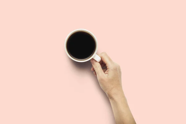 Uma mão está segurando uma xícara com café quente em um fundo rosa. Conceito de pequeno almoço com café ou chá. Bom dia, noite, insónia. Deitado plano, vista superior — Fotografia de Stock