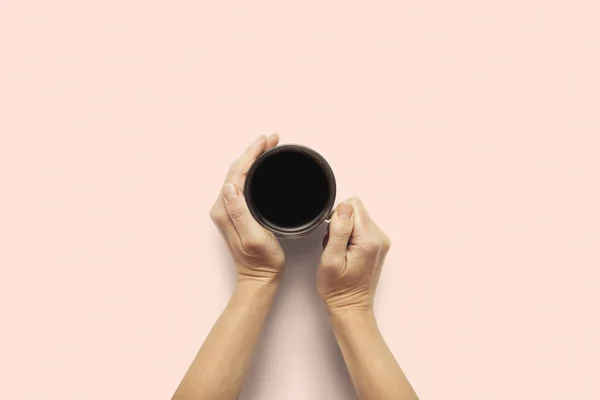 Duas mãos segurando uma xícara com café quente em um fundo rosa. Conceito de pequeno almoço com café ou chá. Bom dia, noite, insónia. Deitado plano, vista superior — Fotografia de Stock