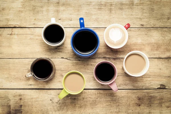 Una gran cantidad de tazas multicolores con café y bebidas de café sobre un fondo de madera. Concepto de desayuno con café, café con amigos. Piso tendido, vista superior — Foto de Stock