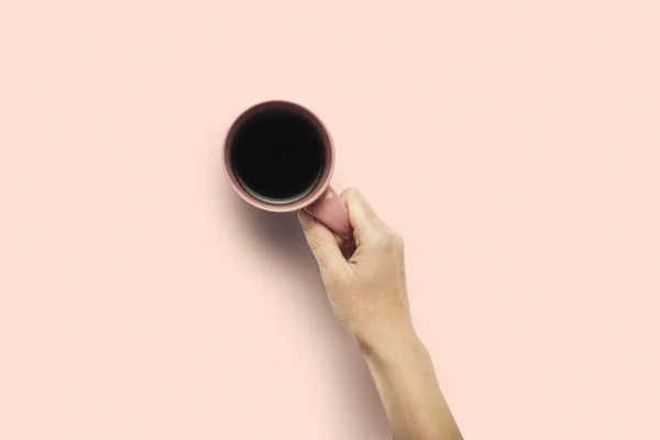 Una mano sostiene una taza con café caliente sobre un fondo rosado. Concepto de desayuno con café o té. Buenos días, noche, insomnio. Piso tendido, vista superior — Foto de Stock