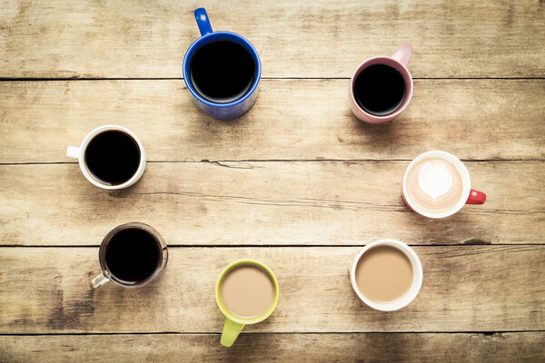 A lot of multicolored cups with coffee and coffee drinks on a wooden background. Ellipse form. Concept breakfast with coffee, coffee with friends. Flat lay, top view