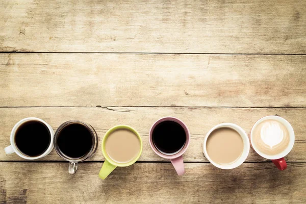 Molte tazze multicolori con bevande di caffè e caffè allineate su uno sfondo di legno. Concetto colazione con caffè, caffè con gli amici. Posa piatta, vista dall'alto — Foto Stock