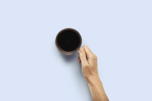 Mano sosteniendo una taza con café caliente sobre un fondo azul. Concepto de desayuno con café o té. Buenos días, noche, insomnio. Piso tendido, vista superior — Foto de Stock