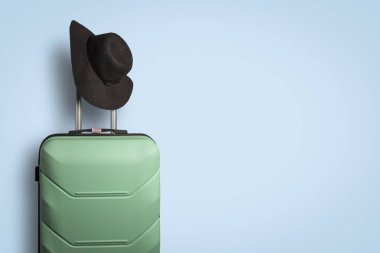Plastic suitcase on wheels and a hat with a wide brim on the handle on a blue background. Travel concept, vacation trip, visit to relatives clipart