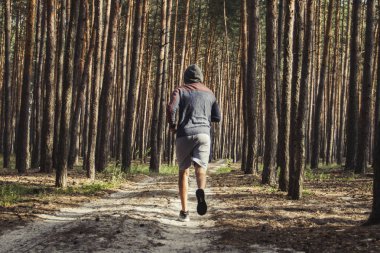 Kapüşonlu adam çam ormanında antrenman yapıyor. Açık havada sabah koşusu kavramı.