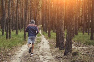 Kapüşonlu adam çam ormanında antrenman yapıyor. Açık havada sabah koşusu kavramı.