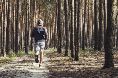 Kapüşonlu adam çam ormanında antrenman yapıyor. Açık havada sabah koşusu kavramı.