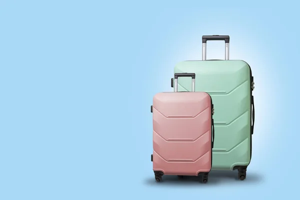 Due valigie su ruote su sfondo blu. Concetto di viaggio, un viaggio di vacanza, una visita ai parenti. Colore rosa e verde — Foto Stock