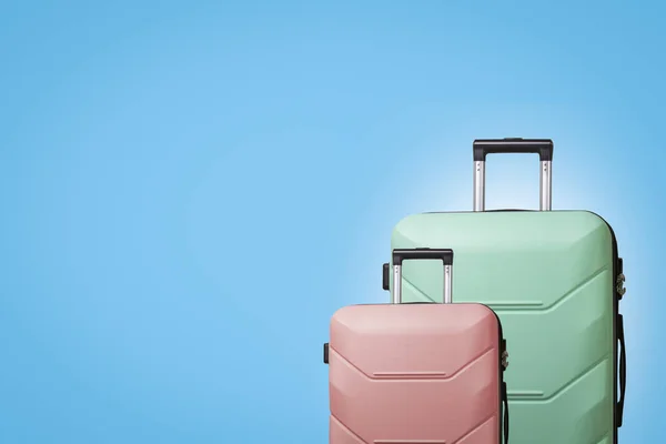 Două valize pe roți pe un fundal albastru. Conceptul de călătorie, o excursie de vacanță, o vizită la rude. Culoare roz și verde — Fotografie, imagine de stoc