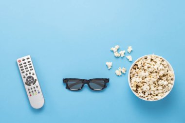Patlamış mısırlı kase, Imax gözlükleri, mavi arka planda televizyon için uzaktan kumanda. Ev sineması kavramı, sinemanın yenilikleri, boş zaman. Düz yatış, üst görünüm