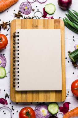Bir kesme tahtası ve bir defter ile kopya alanı etrafında taze çiftlik sebze. Domates, kırmızı soğan, baharat, salatalık, havuç. sahne pişirme
