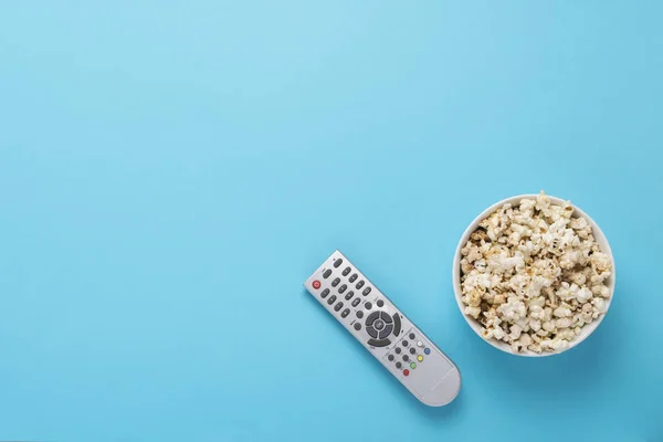 Ciotola con popcorn e telecomando per TV su sfondo blu. Concetto home theater, film, tempo libero. Posa piatta, vista dall'alto — Foto Stock