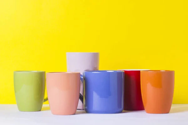 Una gran cantidad de tazas multicolores de café o té sobre un fondo amarillo. El concepto de una empresa amigable, una familia numerosa, reunirse con amigos para una taza de té o café . — Foto de Stock