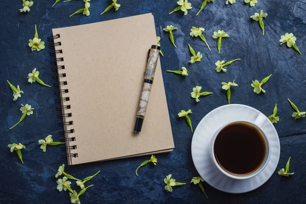 Taza de café, cuaderno y flores sobre un fondo azul oscuro. Piso, vista superior — Foto de Stock