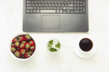 Çalışma alanı. Dizüstü bilgisayar, bir kase çilek, buz ve nane ile serinletici bir içki, bir fincan kahve. Üstten Görünüm, düz yatıyordu.