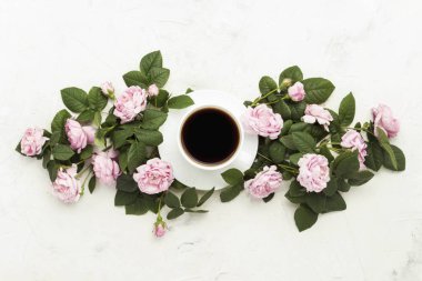 Hafif bir taş zemin üzerine siyah kahve ve pembe güller ile beyaz fincan. Düz yatıyordu, en iyi görünümü