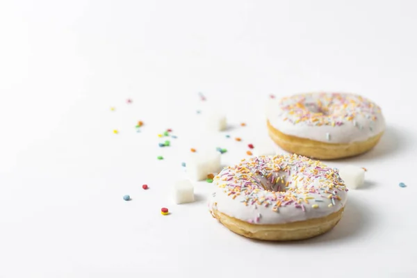 Свежие вкусные пончики и сладкие разноцветные декоративные конфеты на белом фоне. Концепция выпечки, свежая выпечка, вкусный завтрак . — стоковое фото
