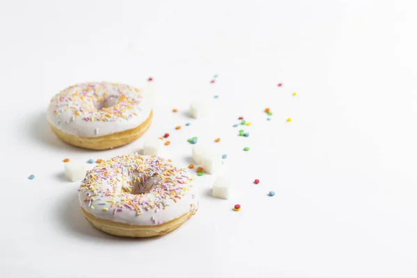 Свежие вкусные пончики и сладкие разноцветные декоративные конфеты на белом фоне. Концепция выпечки, свежая выпечка, вкусный завтрак . — стоковое фото