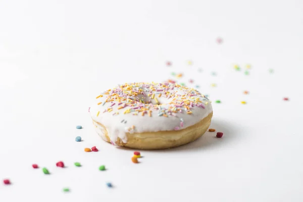 Свежий вкусный пончик и сладкие разноцветные декоративные конфеты на белом фоне. Концепция выпечки, свежая выпечка, вкусный завтрак . — стоковое фото