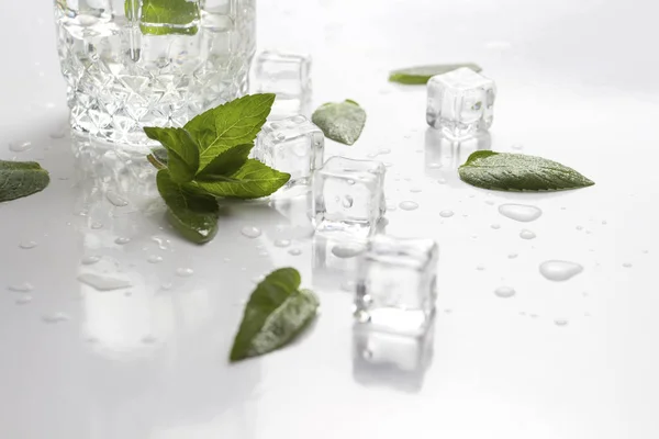 Glas mit erfrischendem Wasser, Minzblättern, Wassertropfen und Eiswürfeln auf hellem Hintergrund — Stockfoto