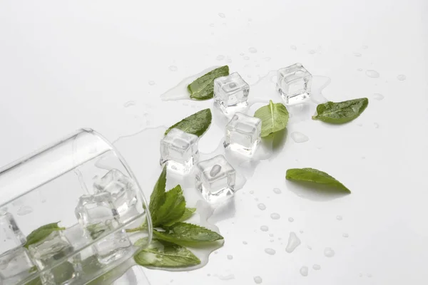Verschüttetes Glas mit erfrischendem Wasser, Minzblättern und Eiswürfeln auf hellem Hintergrund — Stockfoto