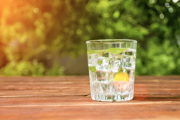 Um copo com uma bebida refrescante fria com gelo e folhas de hortelã em uma mesa de madeira e no fundo do Jardim. Conceito de recreação ao ar livre — Fotografia de Stock