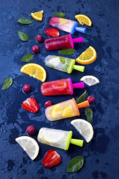 Multicolored bright fruit popsicle with strawberry, cherry, lemon, orange, lemon and mint aroma and fresh fruit on a dark blue background