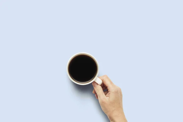 Mano sosteniendo una taza con café caliente sobre un fondo azul. Concepto de desayuno con café o té. Buenos días, noche, insomnio. Piso tendido, vista superior — Foto de Stock